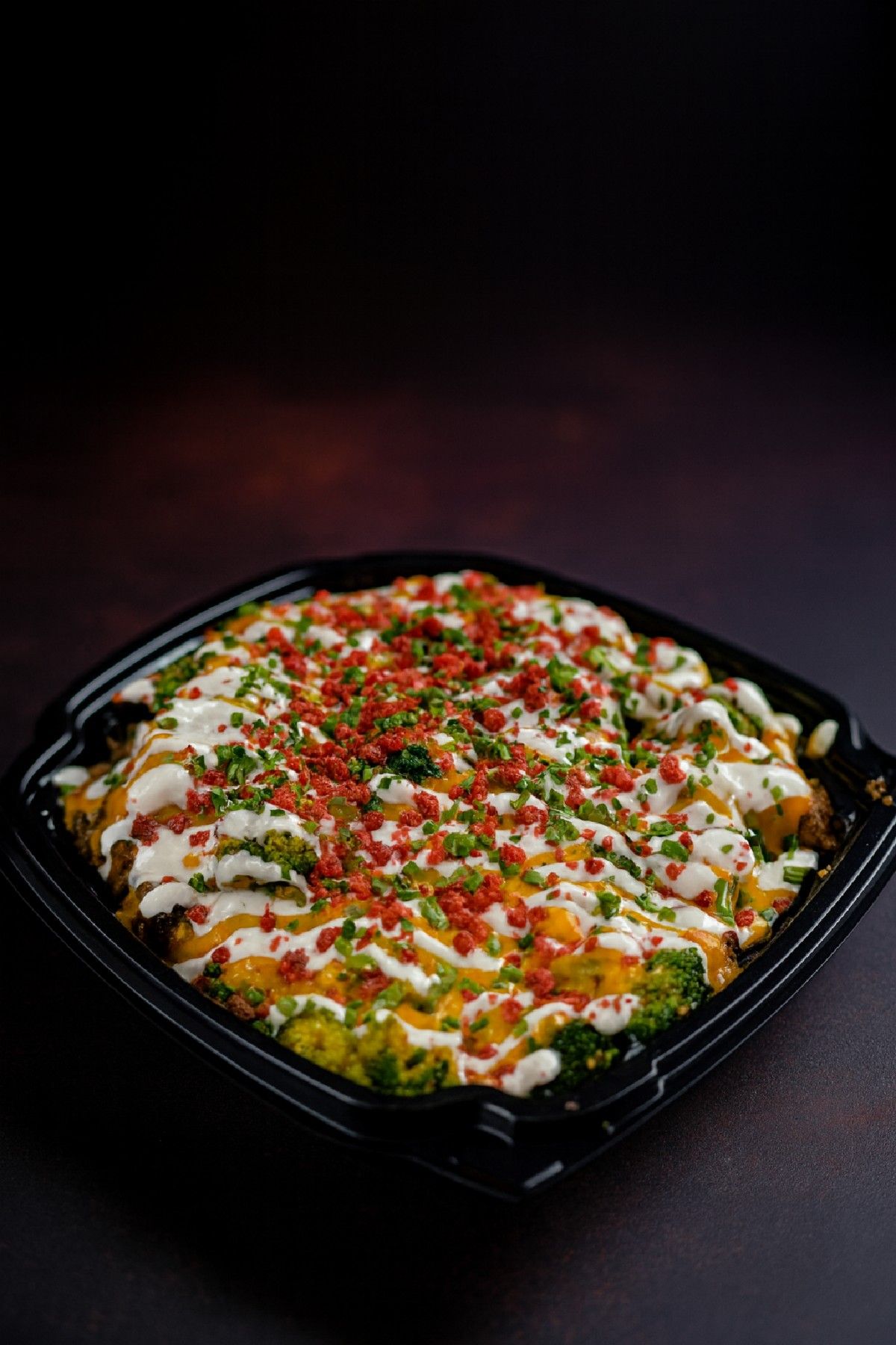 A loaded baked potato topped with cheese, sour cream, chives and bacon bits in a takeout bowl