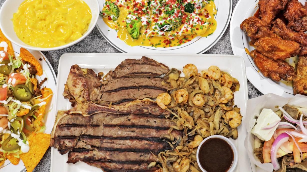 A T-bone steak with sautéed shrimp, peppers and onions, surrounded by nachos, wings and loaded fries